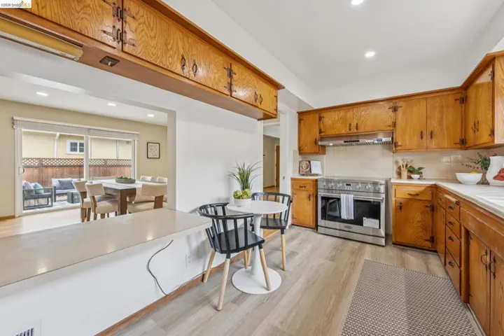 Kitchen featuring wood-finish cabinetry, stainless steel range with hood, light-toned countertops, and wood-finish flooring