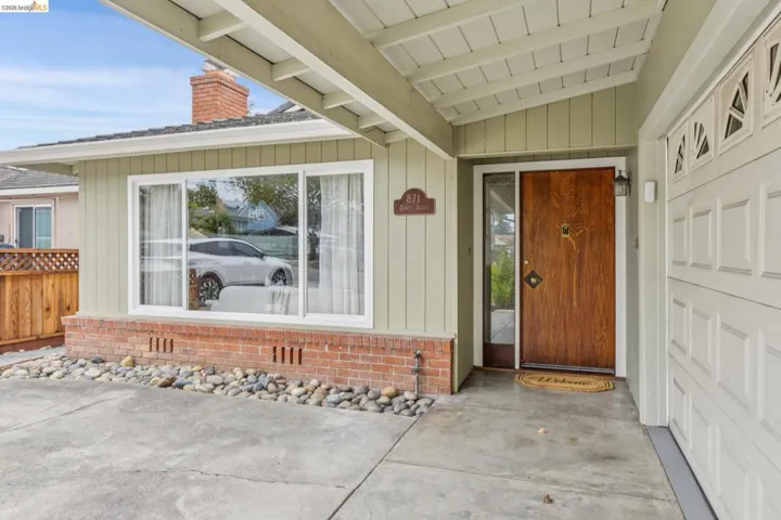 Wood-paneled front door with sidelight, overhead outdoor lighting, and an attached two-car garage