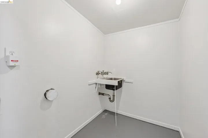 Utility sink with dual faucets, wall-mounted outlets, and gray flooring