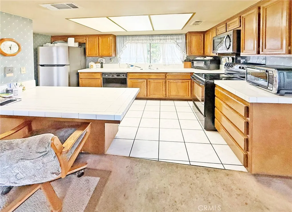 Kitchen has Electric Stove, Built-In Microwave, Dishwasher, Tile Flooring, An Abundance of Natural Wood Cabinetry, and a Walk-In Pantry