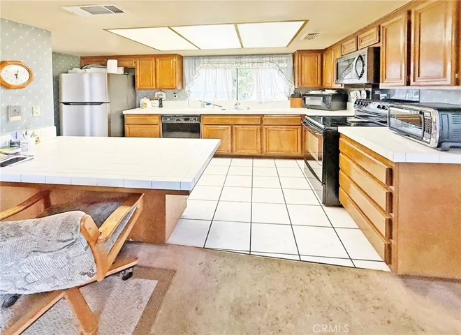 Kitchen has Electric Stove, Built-In Microwave, Dishwasher, Tile Flooring, An Abundance of Natural Wood Cabinetry, and a Walk-In Pantry
