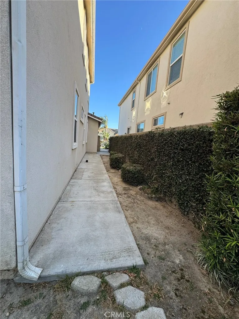 Side Yard – Concrete walkway along the side of the home with mature privacy hedges and access between the front and rear yard.