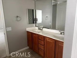 Bathroom featuring dual-sink vanity, wood cabinetry, large mirror, and tile flooring.