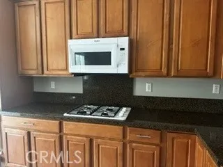 granite , wood cabinetry, gas cooktop, and built-in microwave.