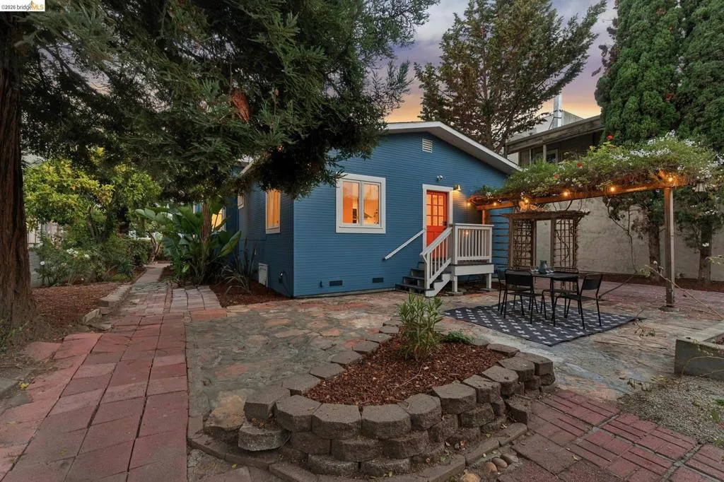 Blue exterior siding, white trim windows, red entry door, wooden pergola, and a stone paver patio