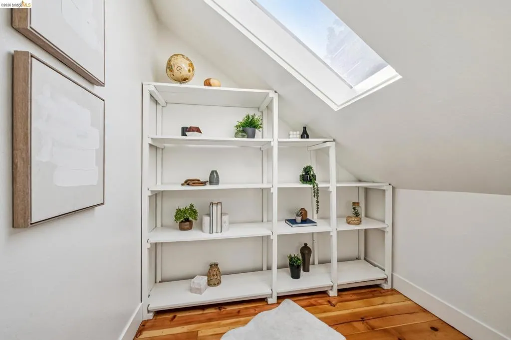 Sloped ceiling with an integrated skylight, light wood-finish flooring, and white built-in shelving