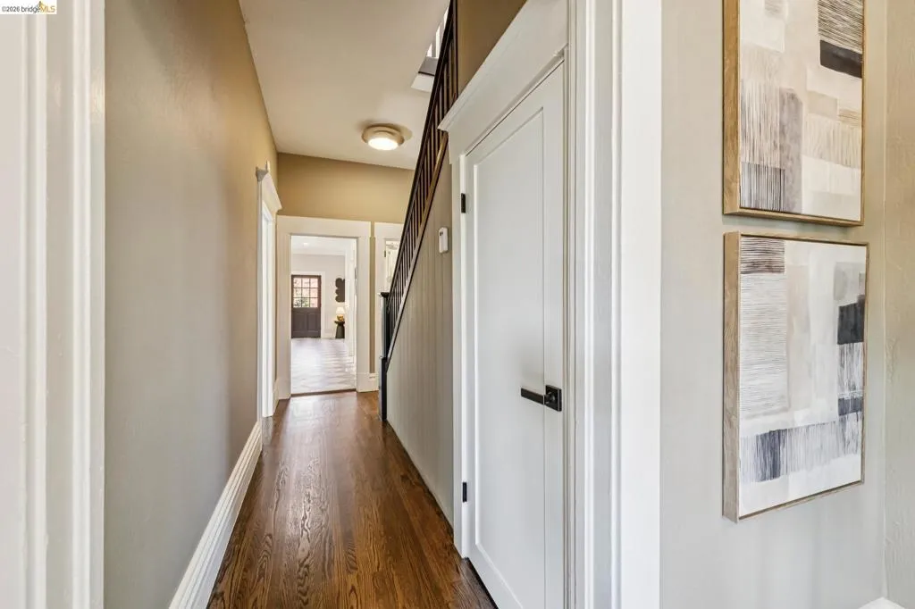 Wood-finish flooring, white panel doors with dark hardware, and a staircase with dark railings