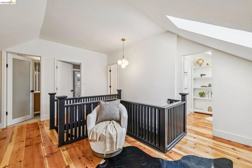 Hardwood flooring, black railing, modern pendant light fixture, white walls, and an integrated skylight