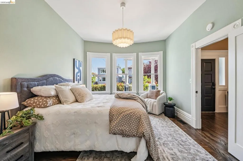 Bay window with three distinct panes, hardwood flooring, decorative ceiling light fixture, detailed white trim, and a paneled dark door