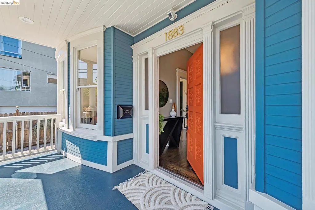 Welcoming entryway featuring a vibrant orange door, white trim, side windows, house numbers, and a recessed mailbox