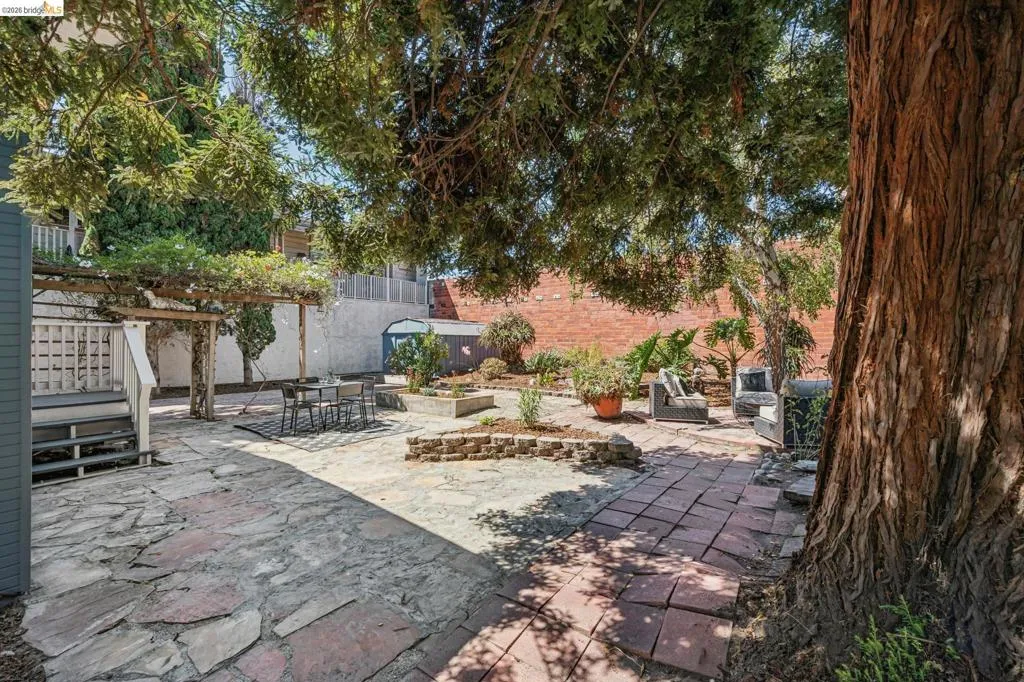 Expansive outdoor space featuring a large mature tree, pergola structure, flagstone patio, brick paver path, and raised planter beds
