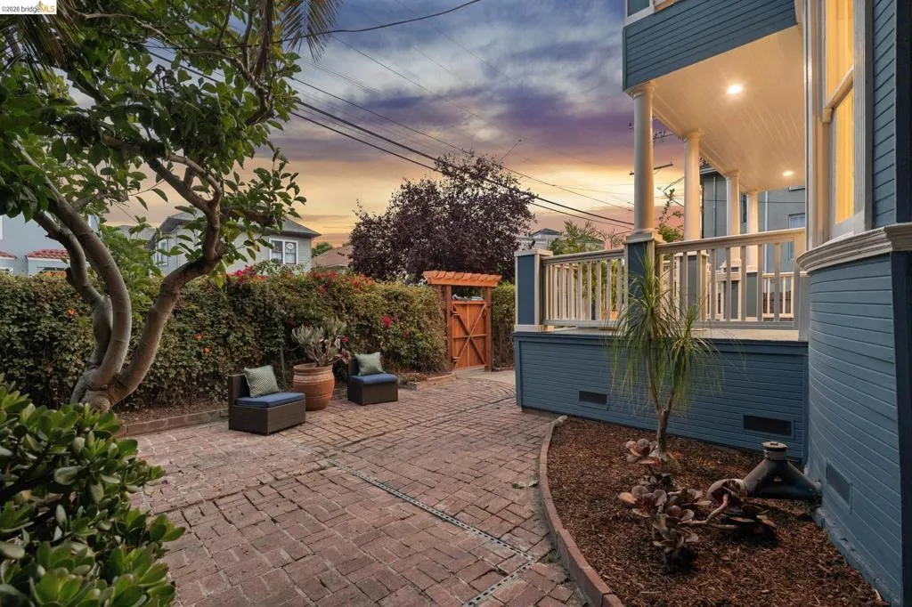Brick paver patio, mature landscaping, wood trellis gate, covered porch with recessed lighting, and white railings