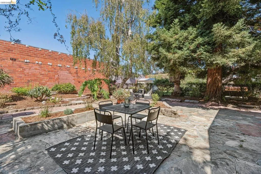 Expansive outdoor patio featuring flagstone paving, layered garden beds with mature plantings, and a prominent brick retaining wall