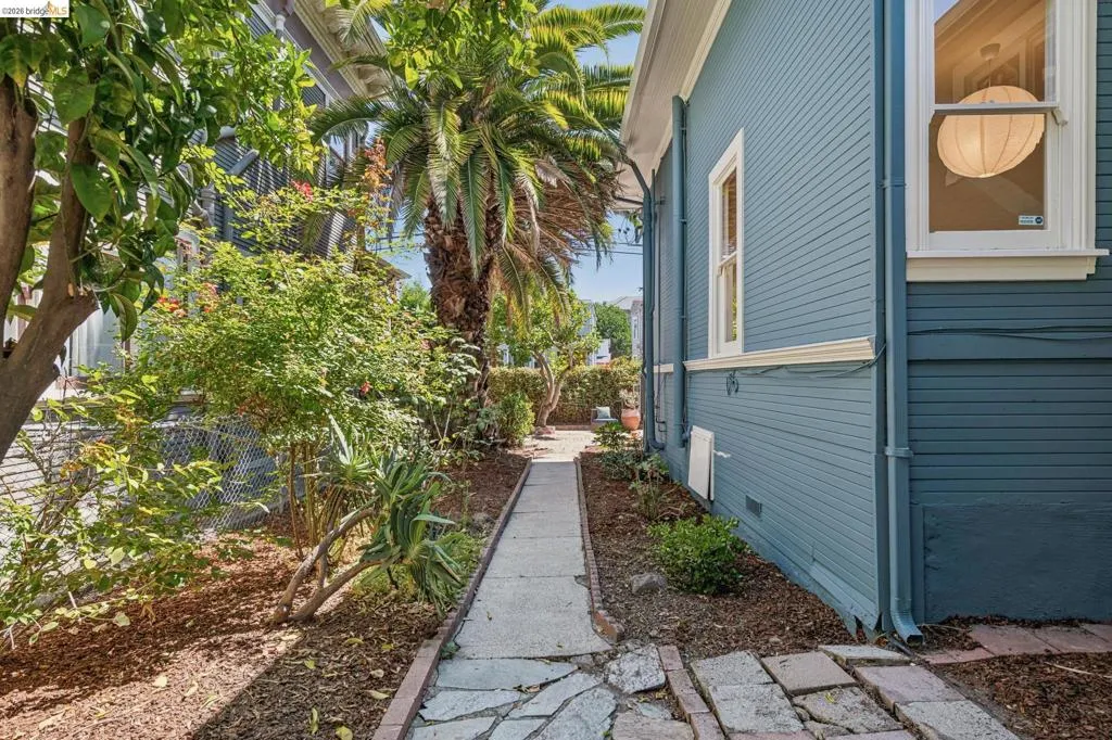 Charming side yard entry featuring a linear stone walkway bordered by mature landscaping, lush tropical plantings, and natural mulch beds