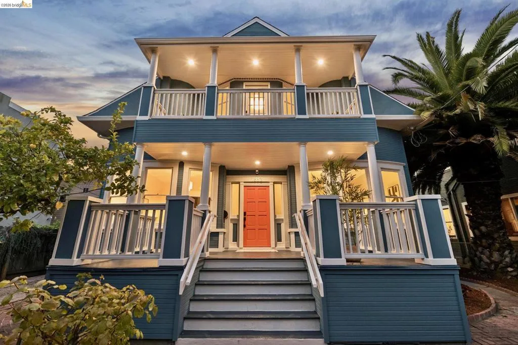 Multi-story property featuring a coral entry door, two-story columns, and a second-story balcony