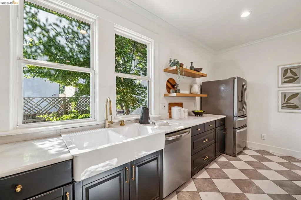 White farmhouse sink with a gold-tone faucet, dark cabinetry, and light countertops