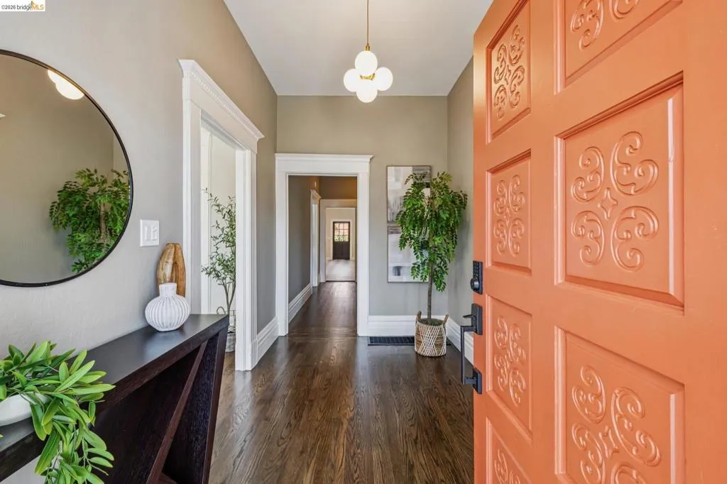 Inviting entry featuring a vibrant orange door with decorative paneling, dark wood-finish flooring, a contemporary console table, and a modern ceiling light fixture