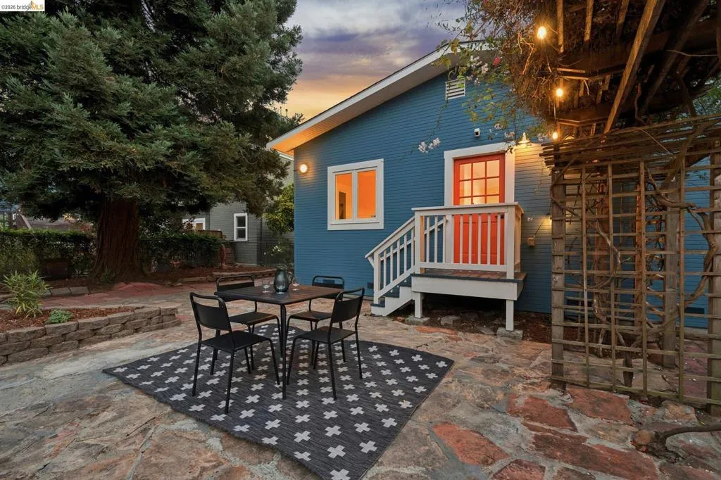 Exterior featuring a blue facade, a vibrant orange entry door, white trim, a stone patio, and a wooden pergola structure