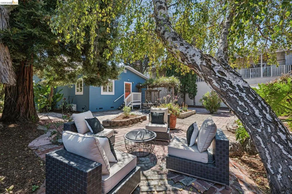 Patio with brick pavers, raised garden beds, mature trees, and a blue exterior structure