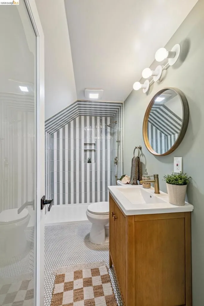 Wood-finish vanity with an integrated sink, polished brass-finish faucet, and a circular mirror