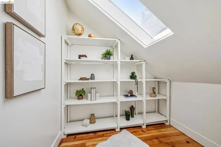 Sloped ceiling with an integrated skylight, light wood-finish flooring, and white built-in shelving