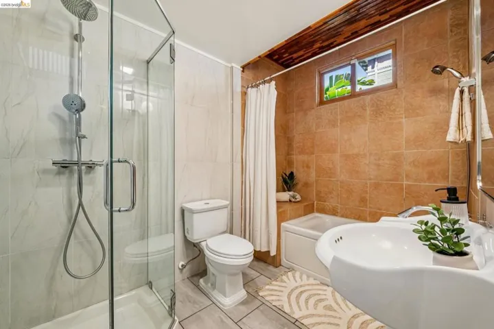 Glass-enclosed shower with rain shower head, separate bathtub with tiled surround, wall-mounted sink, and tiled flooring