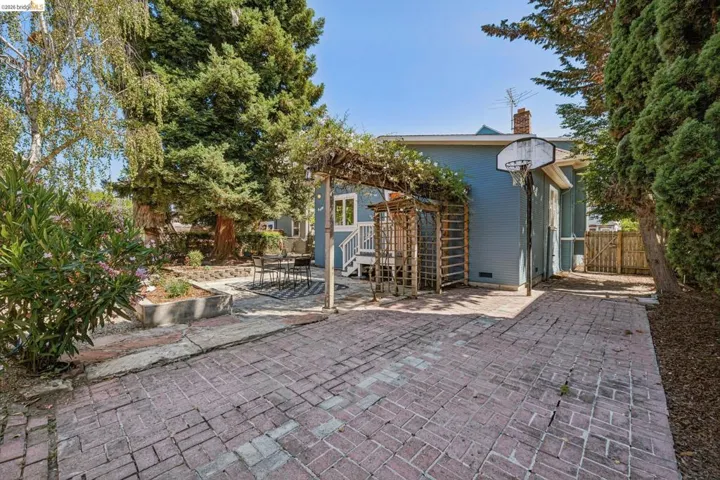 Brick paver patio with a pergola, raised garden bed, mature trees, and fencing
