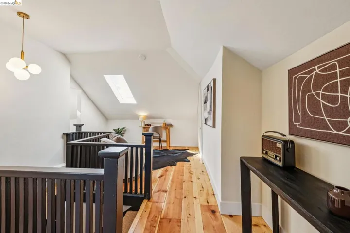 Vaulted ceiling, skylight, wood-finish flooring, dark wood railing, and modern pendant lighting