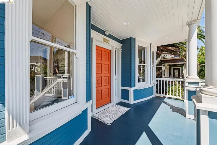 Covered front porch featuring a vibrant orange entry door, white fluted columns, and a beadboard ceiling