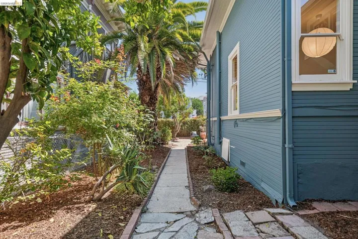 Charming side yard entry featuring a linear stone walkway bordered by mature landscaping, lush tropical plantings, and natural mulch beds