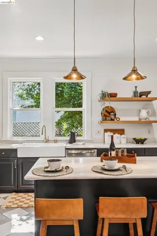 Kitchen featuring a farmhouse sink, dark cabinetry, light-toned countertops, open shelving, and pendant lighting