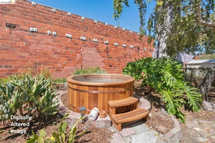 Outdoor wood-plank hot tub with brick surround, complemented by a mature tree and lush landscaping