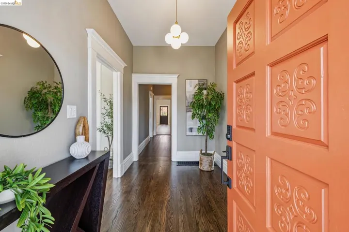 Inviting entry featuring a vibrant orange door with decorative paneling, dark wood-finish flooring, a contemporary console table, and a modern ceiling light fixture
