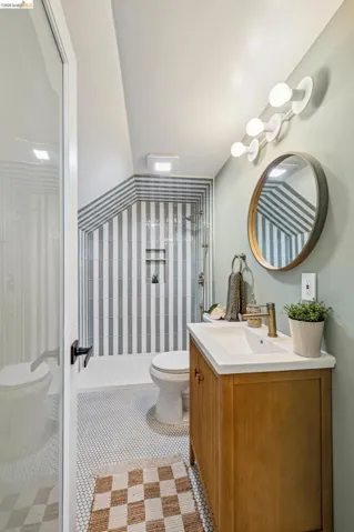 Wood-finish vanity with an integrated sink, polished brass-finish faucet, and a circular mirror