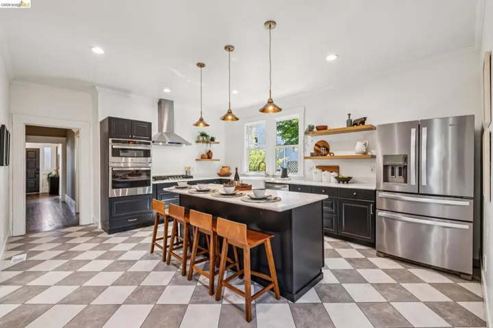 Spacious kitchen featuring stainless steel appliances, a center island with pendant lighting, dark cabinetry, and checkerboard floor tiling