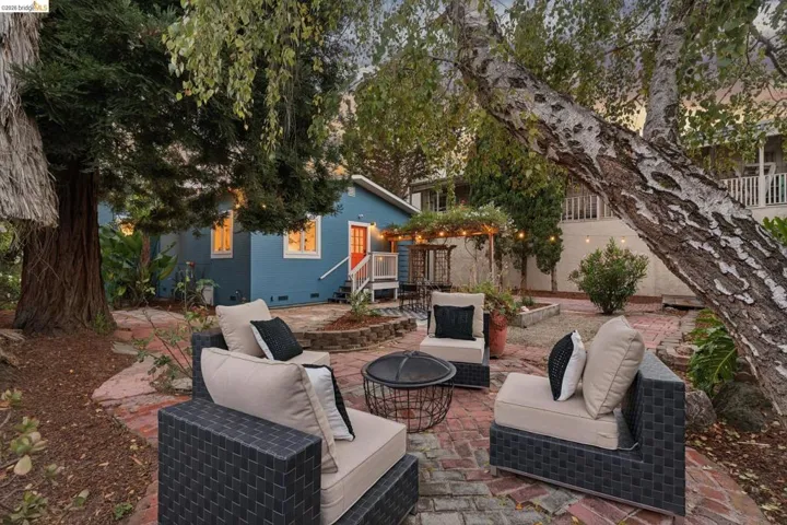 Spacious outdoor patio with a brick-laid surface, shaded by mature trees, and featuring a built-in pergola