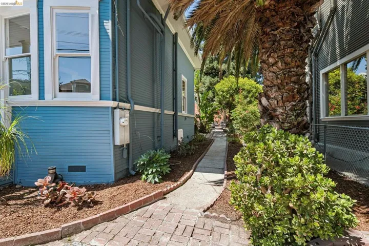 Exterior with blue siding, white window trim, mature palm tree, brick paver pathway, and landscaping with ground cover