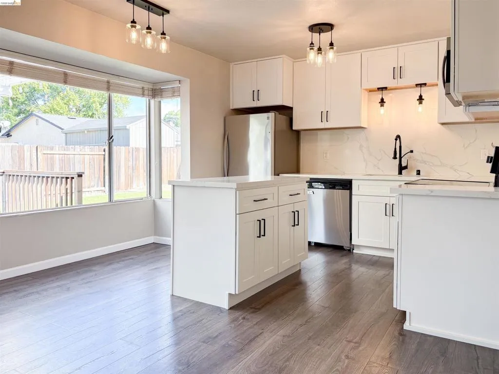 Kitchen featuring white cabinetry, wood-finish flooring, a central island, stainless steel appliances, and a bay window