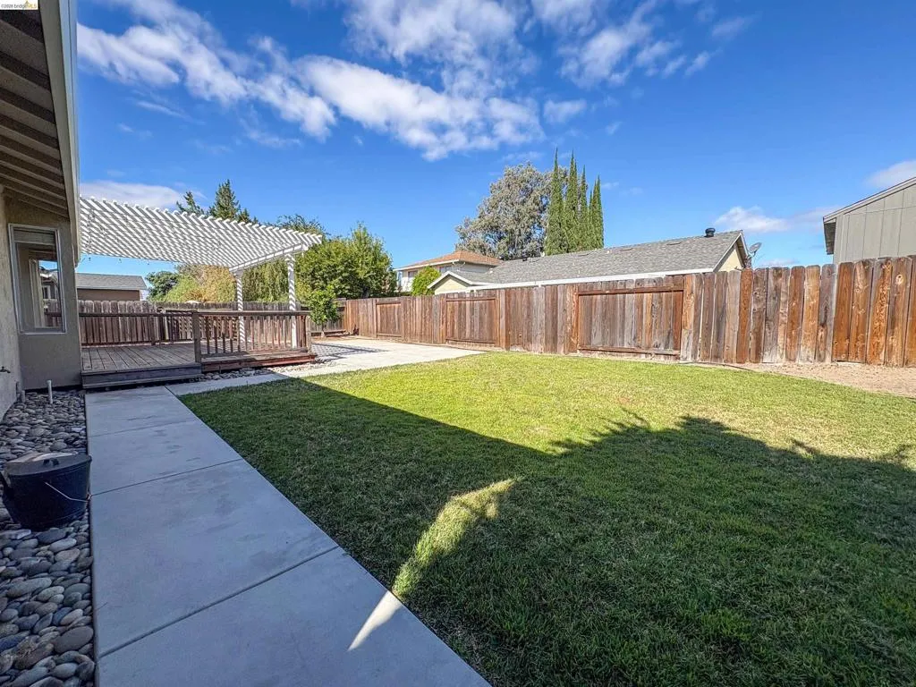 Expansive backyard featuring a wood deck, white pergola, concrete patio, and a manicured lawn