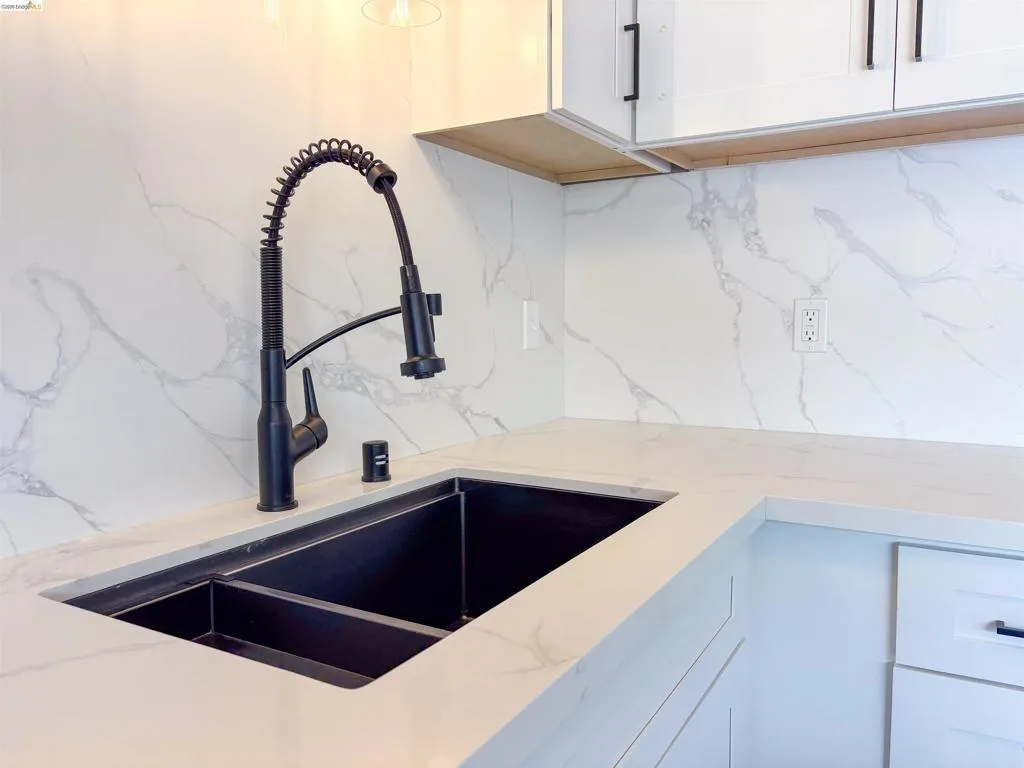 White upper and lower cabinetry with matte black hardware, dual-basin black sink, pull-down faucet, and light-toned countertops with a matching backsplash