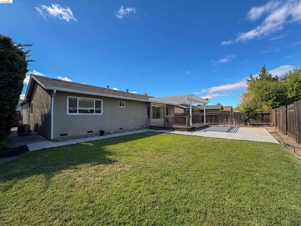 Expansive grass lawn, wood deck with a pergola, concrete patio, and perimeter wood fencing