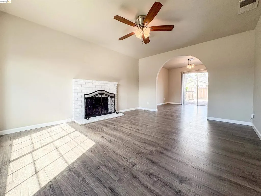 Wood-finish flooring, white brick fireplace, arched doorway, and a ceiling fan with integrated lighting