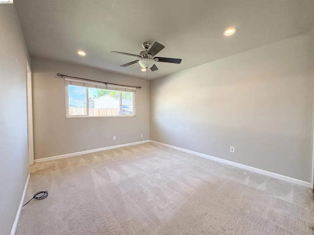 Soft neutral wall paint, recessed lighting, ceiling fan with light fixture, window with roller shades, and plush carpeting