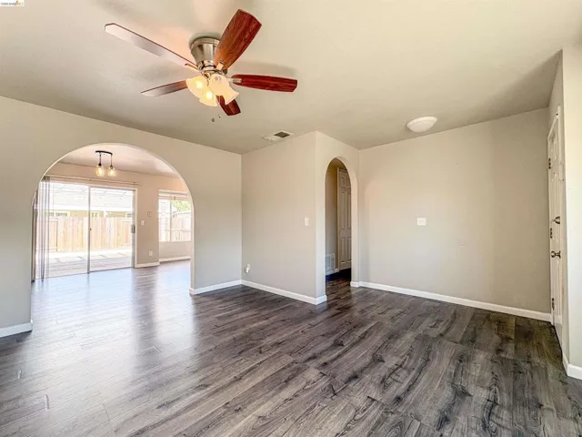 Wood-finish flooring throughout, arched doorways, a ceiling fan with integrated lighting, and sliding glass doors