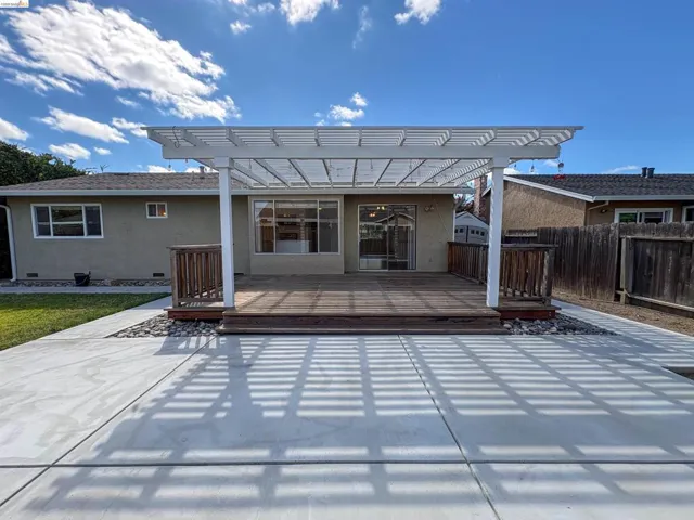 Expansive concrete patio with a wooden deck, covered by a white pergola