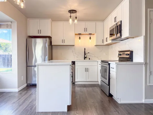 White cabinetry with black hardware, stainless steel appliances, a center island, and wood-finish flooring