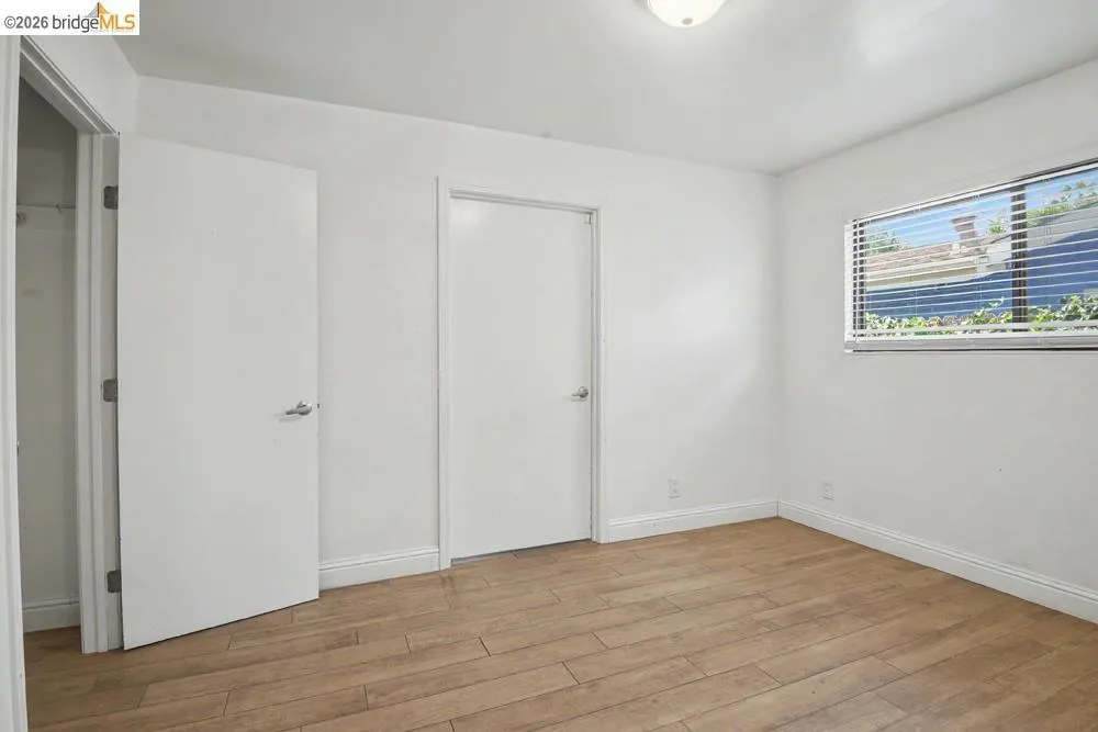 Wood-finish flooring, white walls, and a fixed window with horizontal blinds