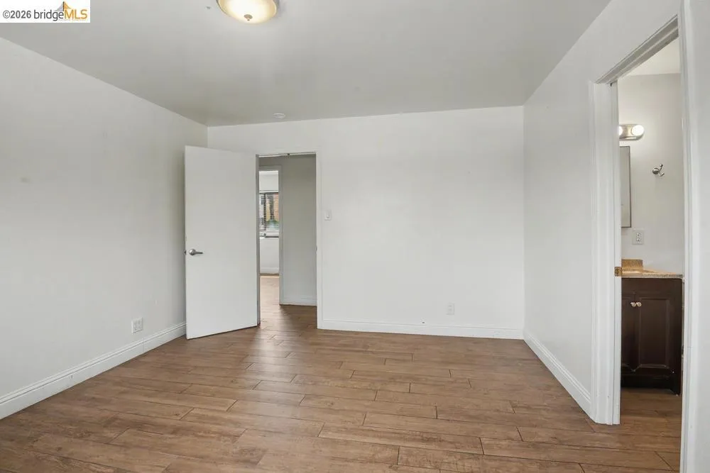 Wood-finish flooring with white baseboards, a flush-mount ceiling light, and an open doorway revealing a vanity with a countertop