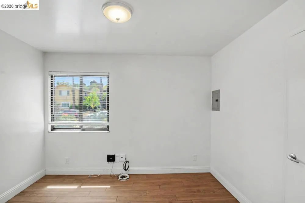 Wood-finish flooring with white baseboards, a window with blinds, and a flush-mount ceiling light