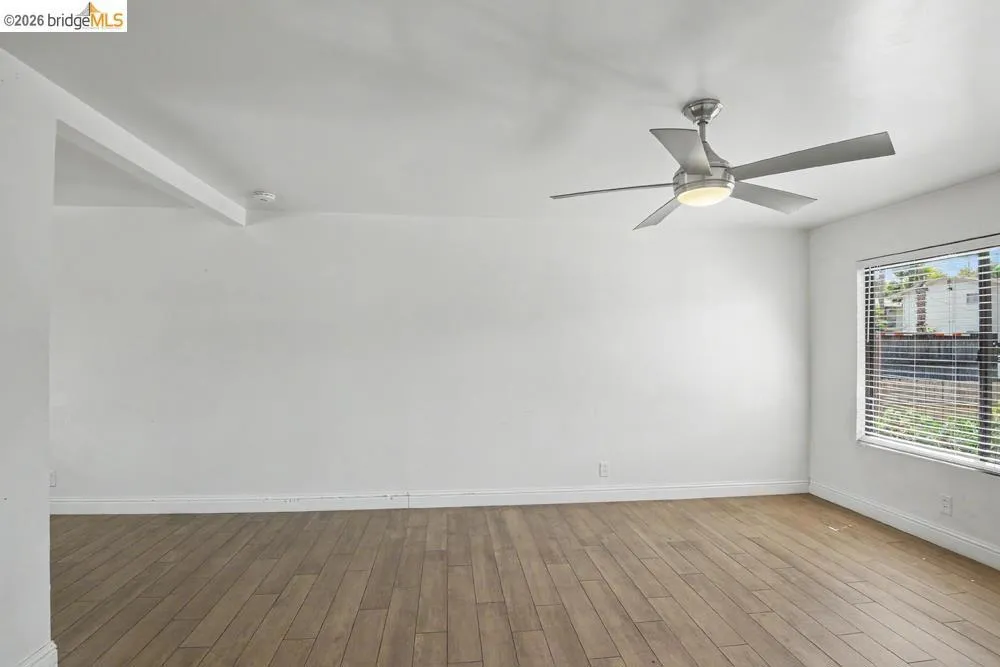 Wood-finish flooring, ceiling fan with integrated lighting, window with blinds, and clean white walls